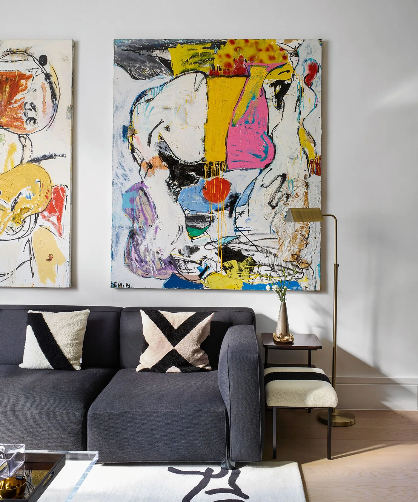 Living room with a dark gray sofa, large colorful abstract artwork, black-and-white cushions and a slim floor lamp.