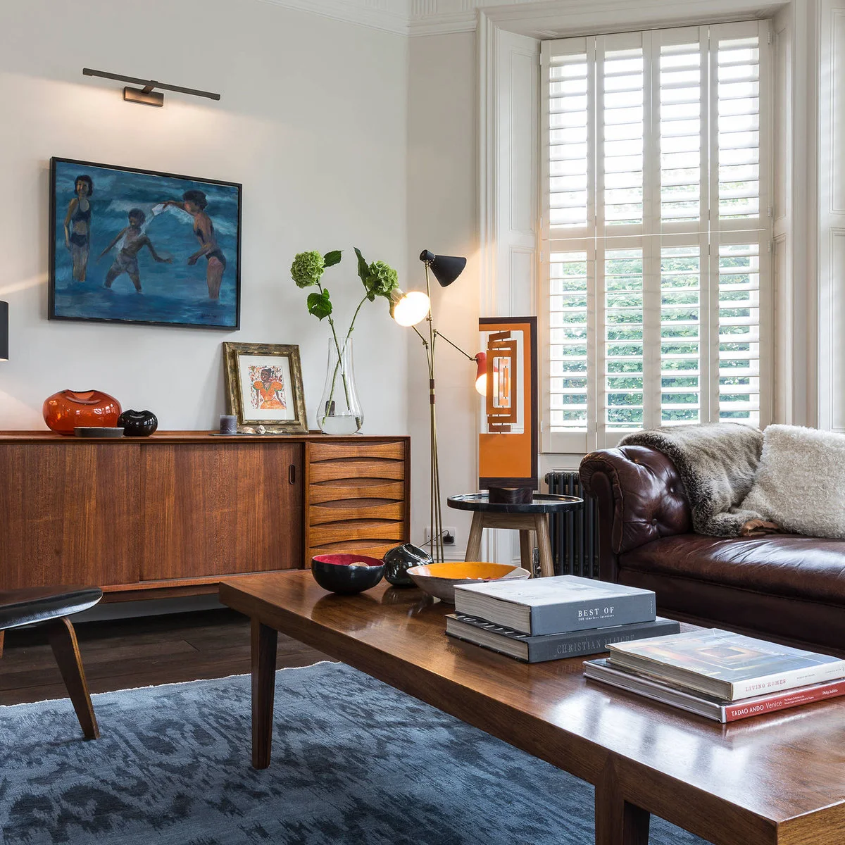 Dark brown tufted leather sofa beside a wood cabinet, blue artwork and a patterned blue rug.