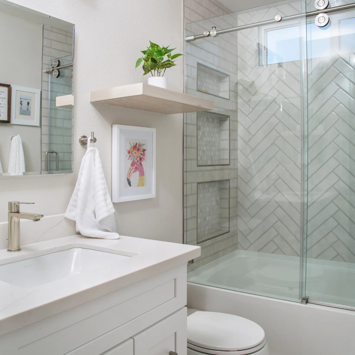 Small bathroom with a white vanity beside a tub enclosed by sliding glass and herringbone wall tiles