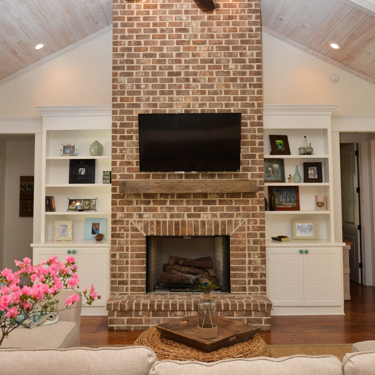 A mixed red-brown brick chimney with a weathered wood mantel stands between pale shelves above a raised brick hearth.