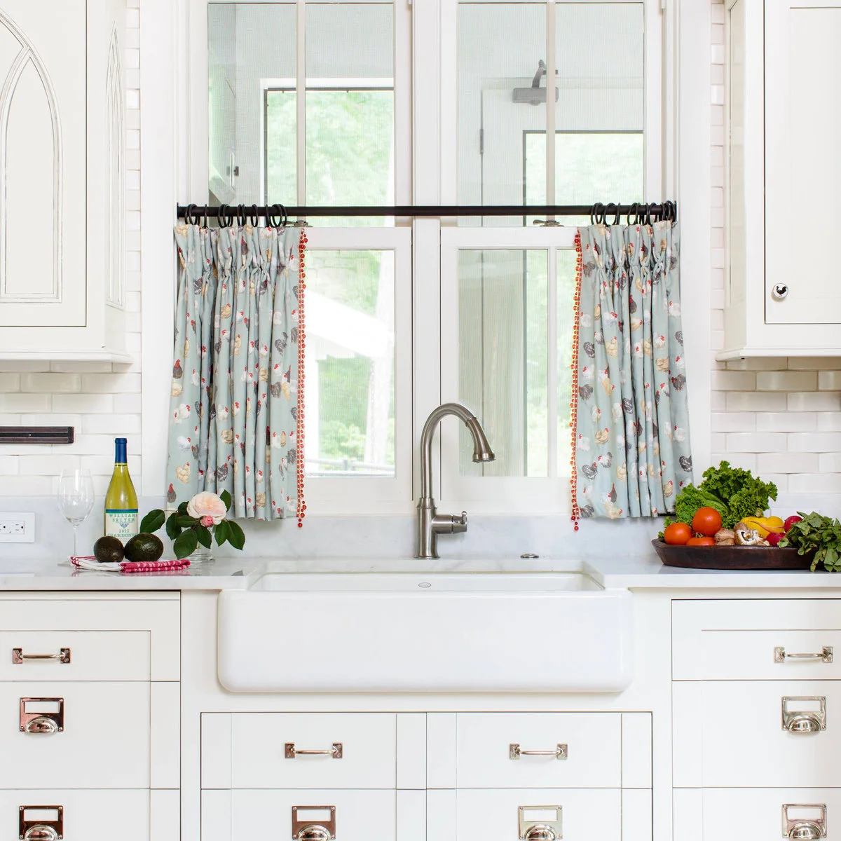 Pale blue floral café curtains with red trim beside a white farmhouse sink