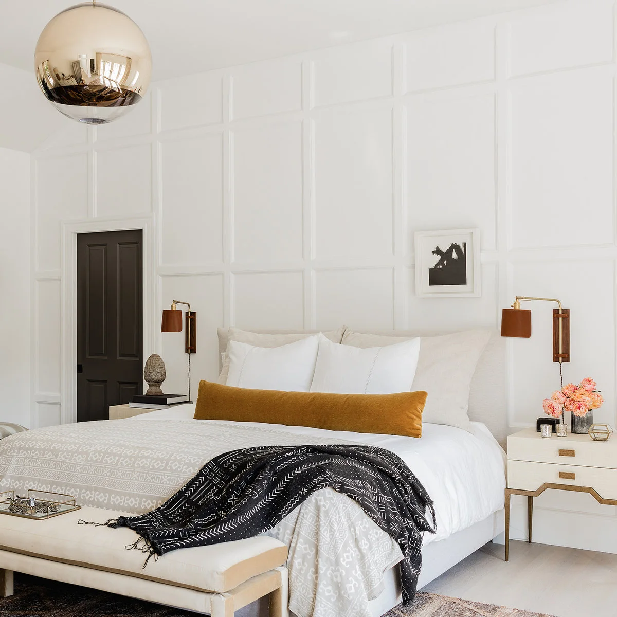 Small white-framed monochrome picture set to one side above a white bed on a paneled wall.