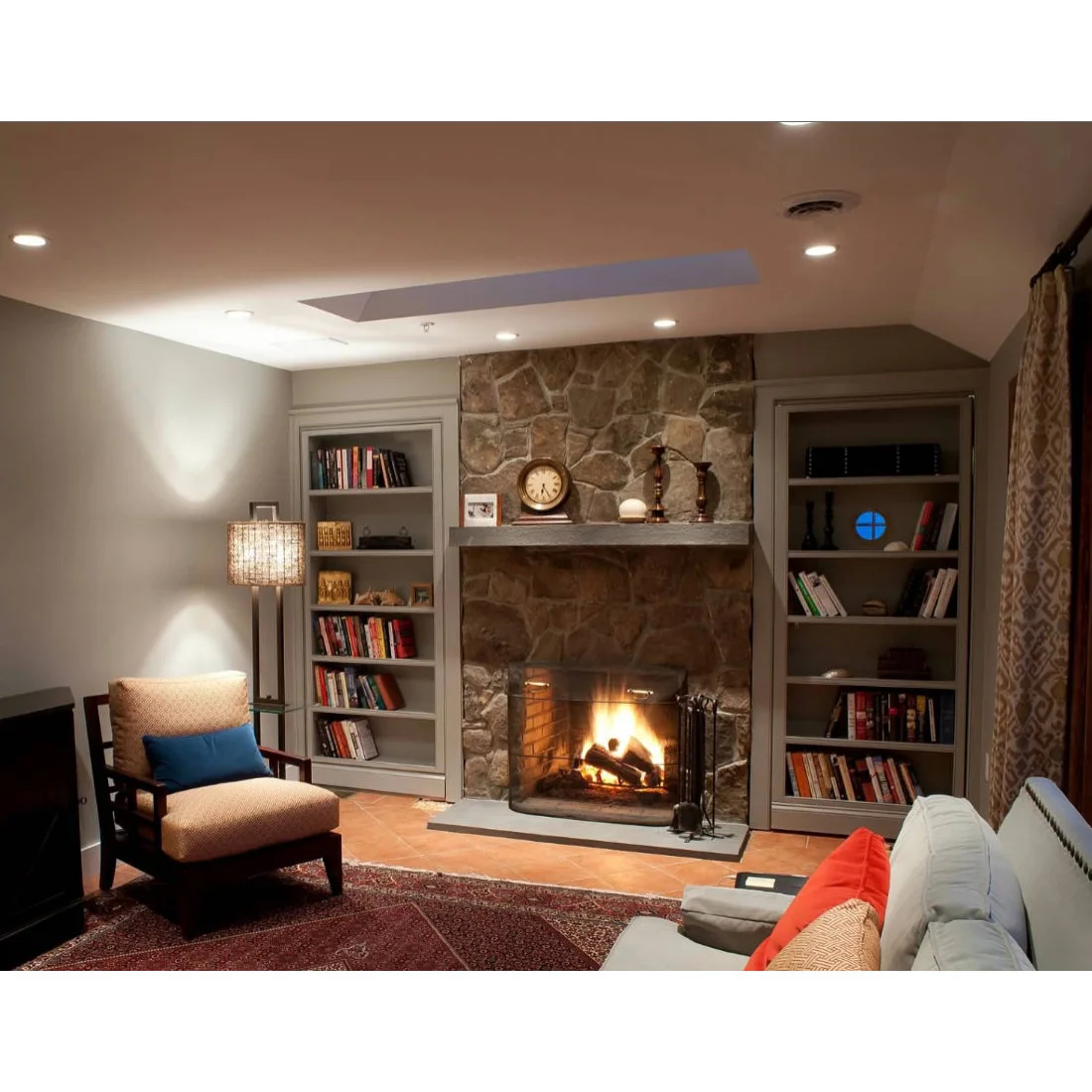 Terracotta tiles surround a gray hearth in front of a stone fireplace with built-in bookshelves.
