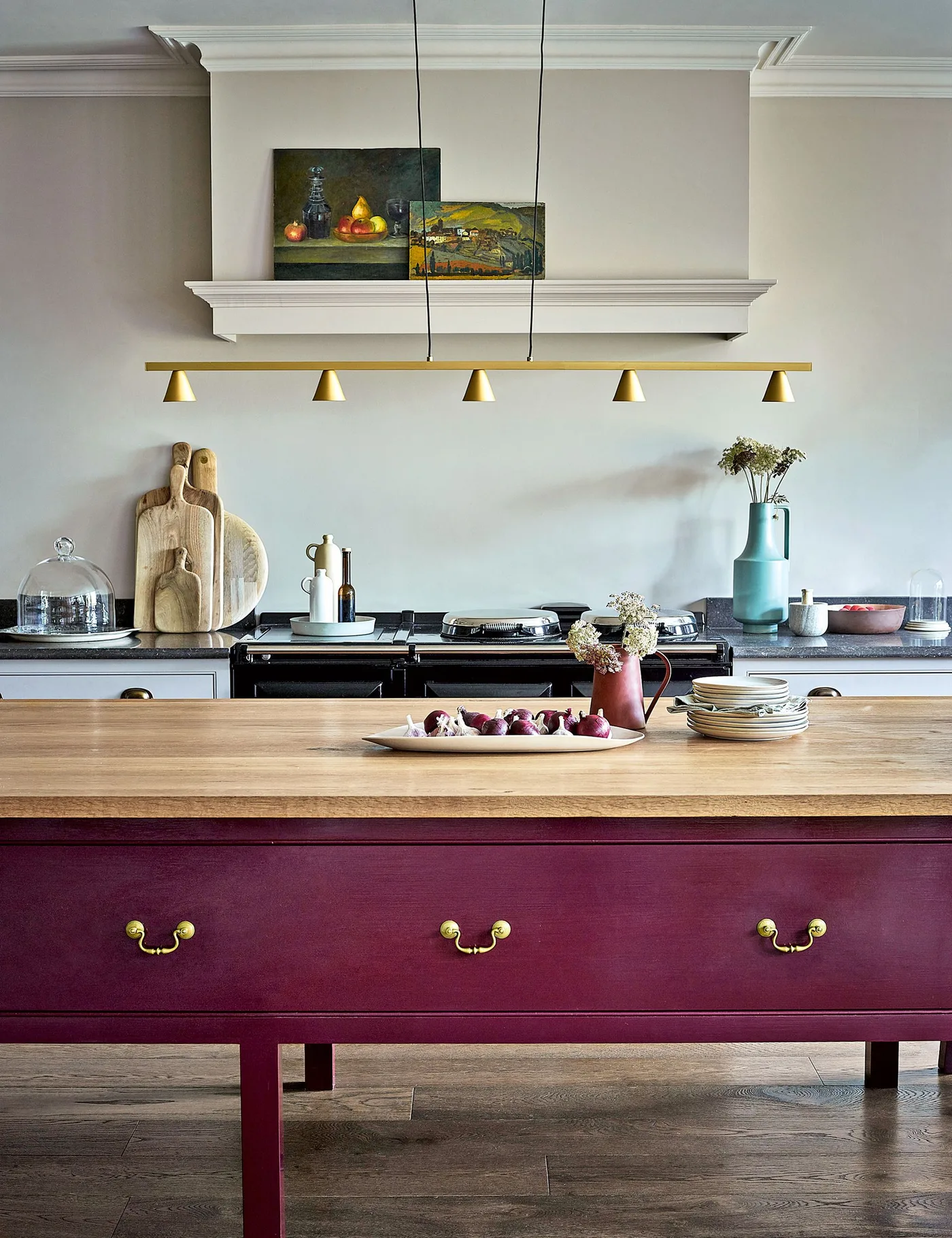 Kitchen with purple island, wooden top, pale cooking wall, black range and linear hanging light.