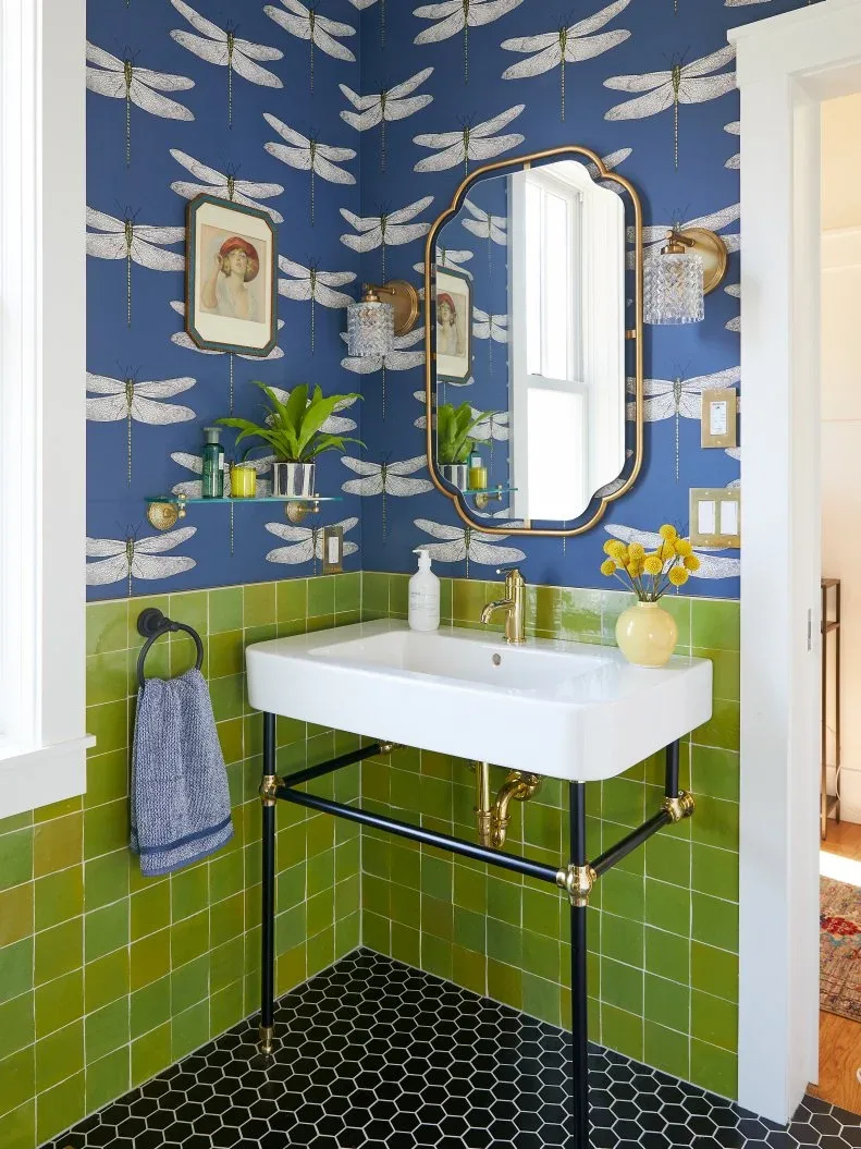 Blue dragonfly wallpaper meets lime green square tiles above a black hexagonal floor, beside a white console basin and shaped warm-metal mirror.