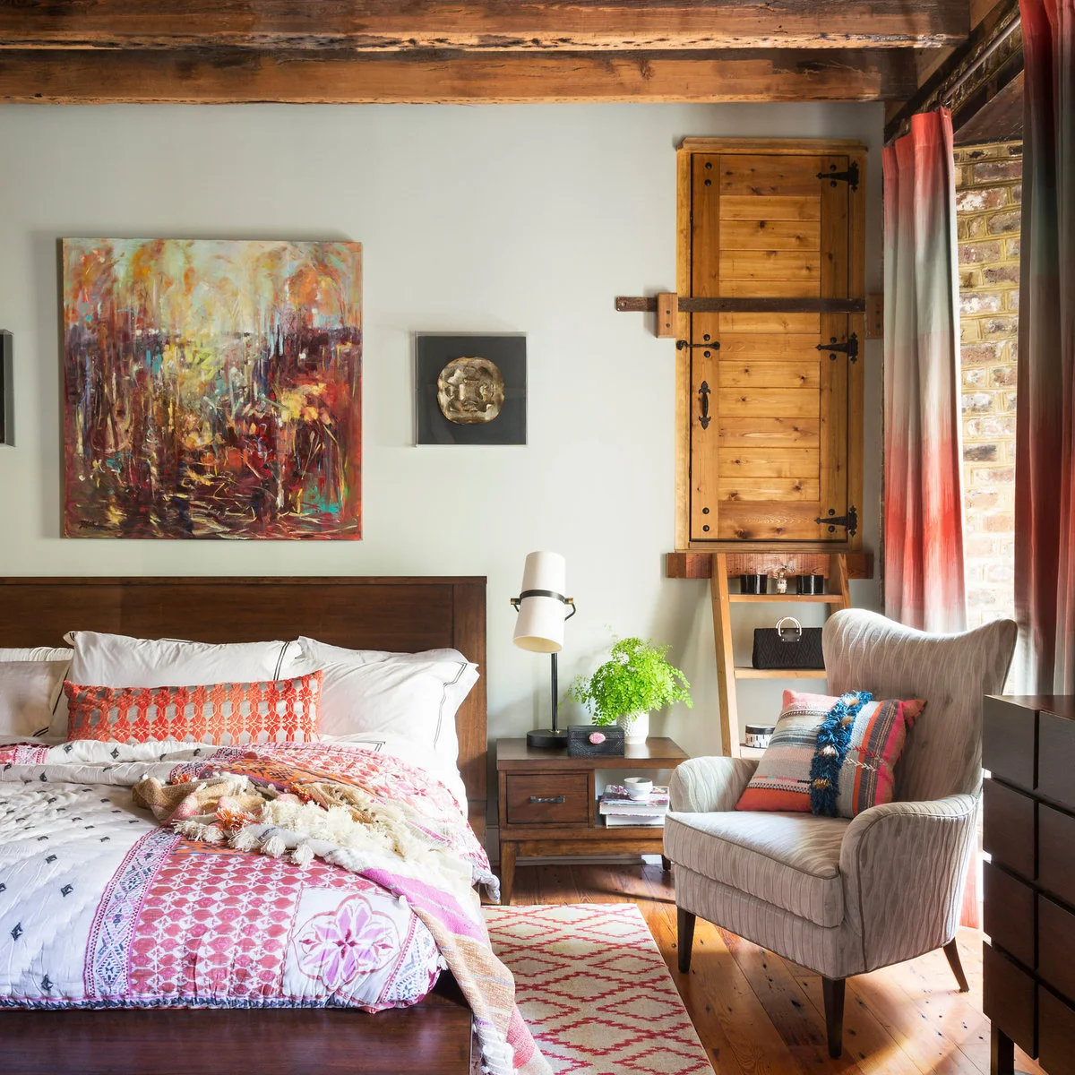 Brown beams and wooden furniture with white bedding, coral textiles and a pale armchair.