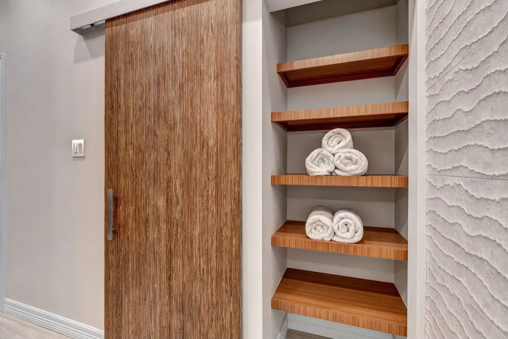 Slim linen recess with wood shelves, rolled white towels and a wood sliding door