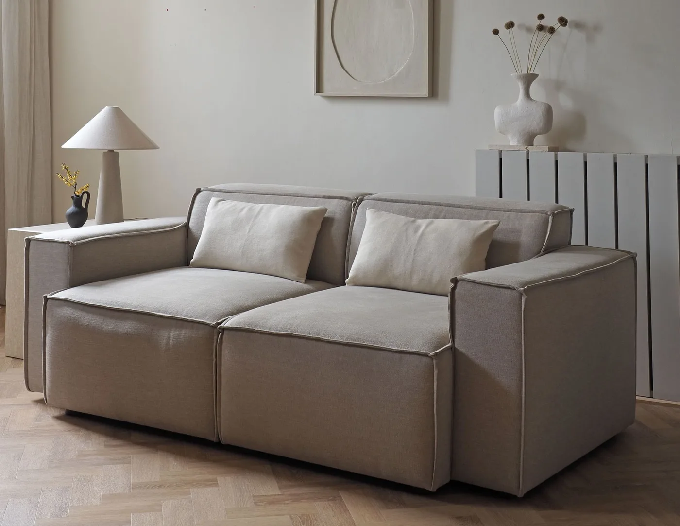 Pale sofa with two understated rectangular pillows against a light wall.