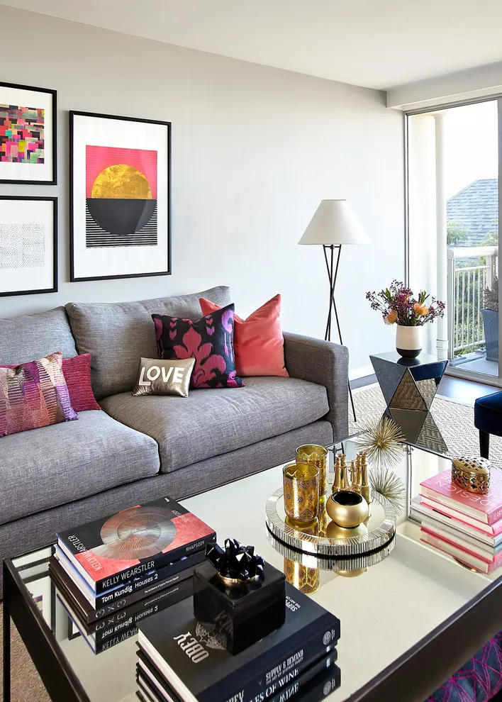 Bright framed prints above a gray sofa with pink and patterned cushions