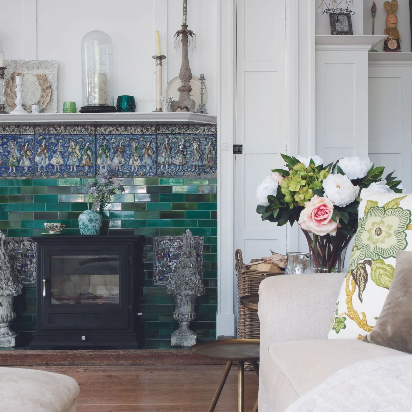 Green rectangular tiles and a blue figurative tile border surround a dark stove against white paneled walls.