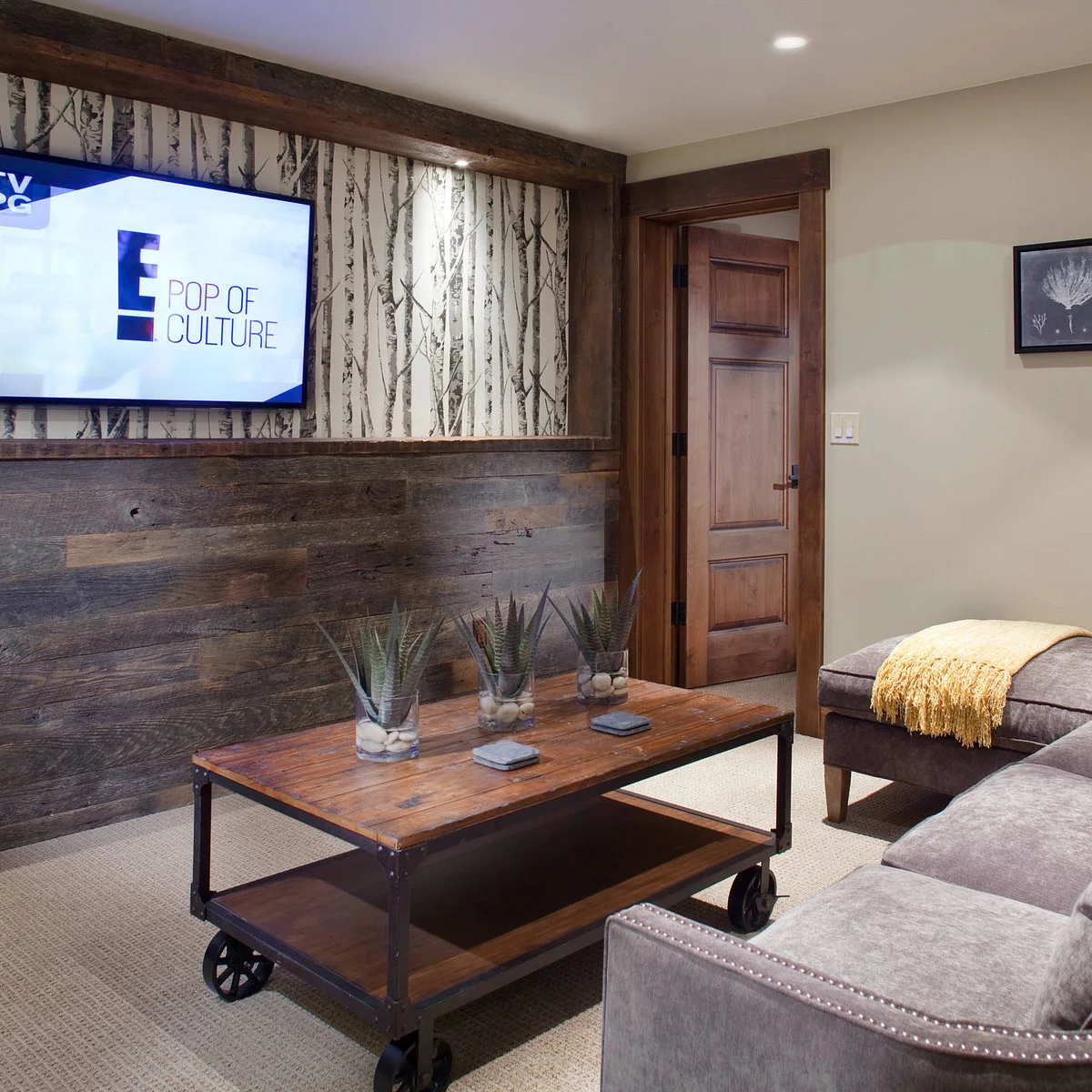 Black-and-white tree wallpaper sits above a wood-clad lower wall behind a TV in a rustic sitting room.
