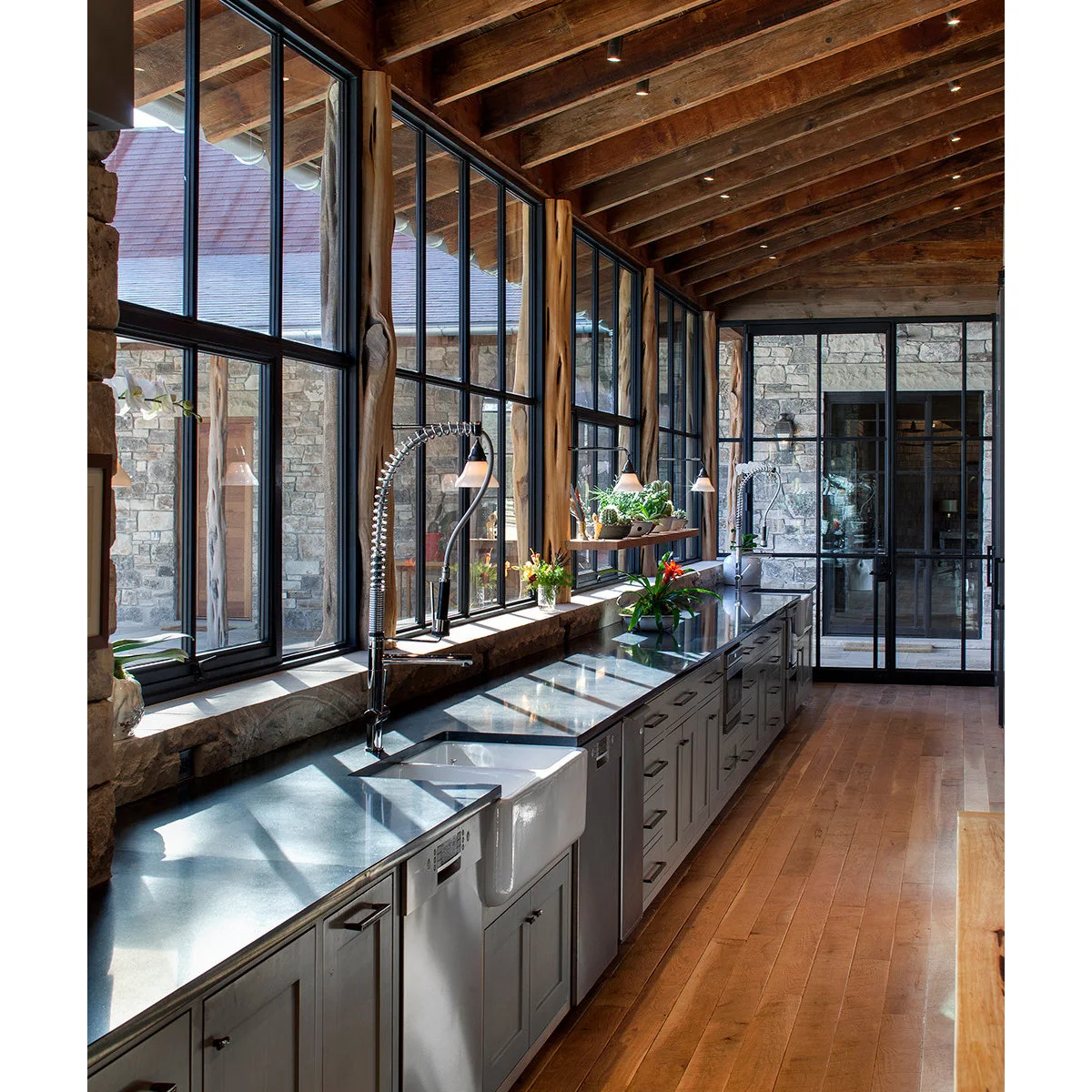Tall dark-framed windows above a long kitchen counter with sinks, small hanging lights and a narrow wood shelf.