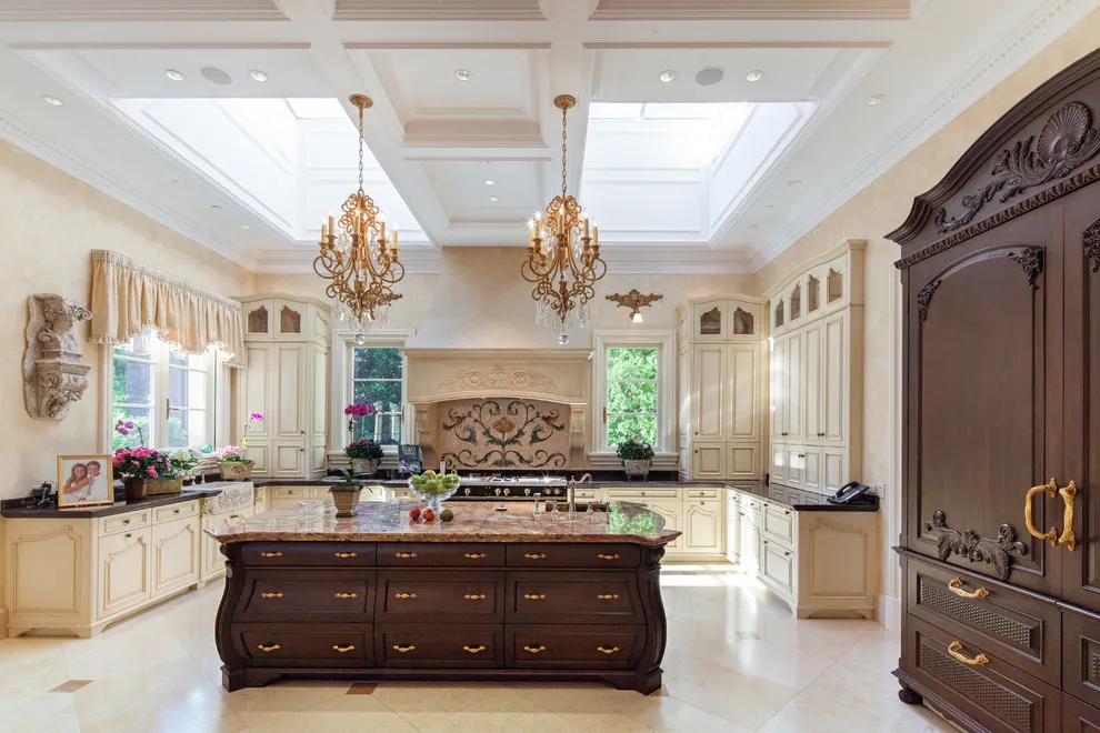 Detailed pale cabinets surround a dark wood island in a room with decorative ceiling lights