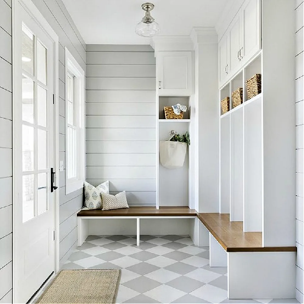 White mudroom cubbies and a wooden corner bench with pale checkerboard flooring beside a glazed door.