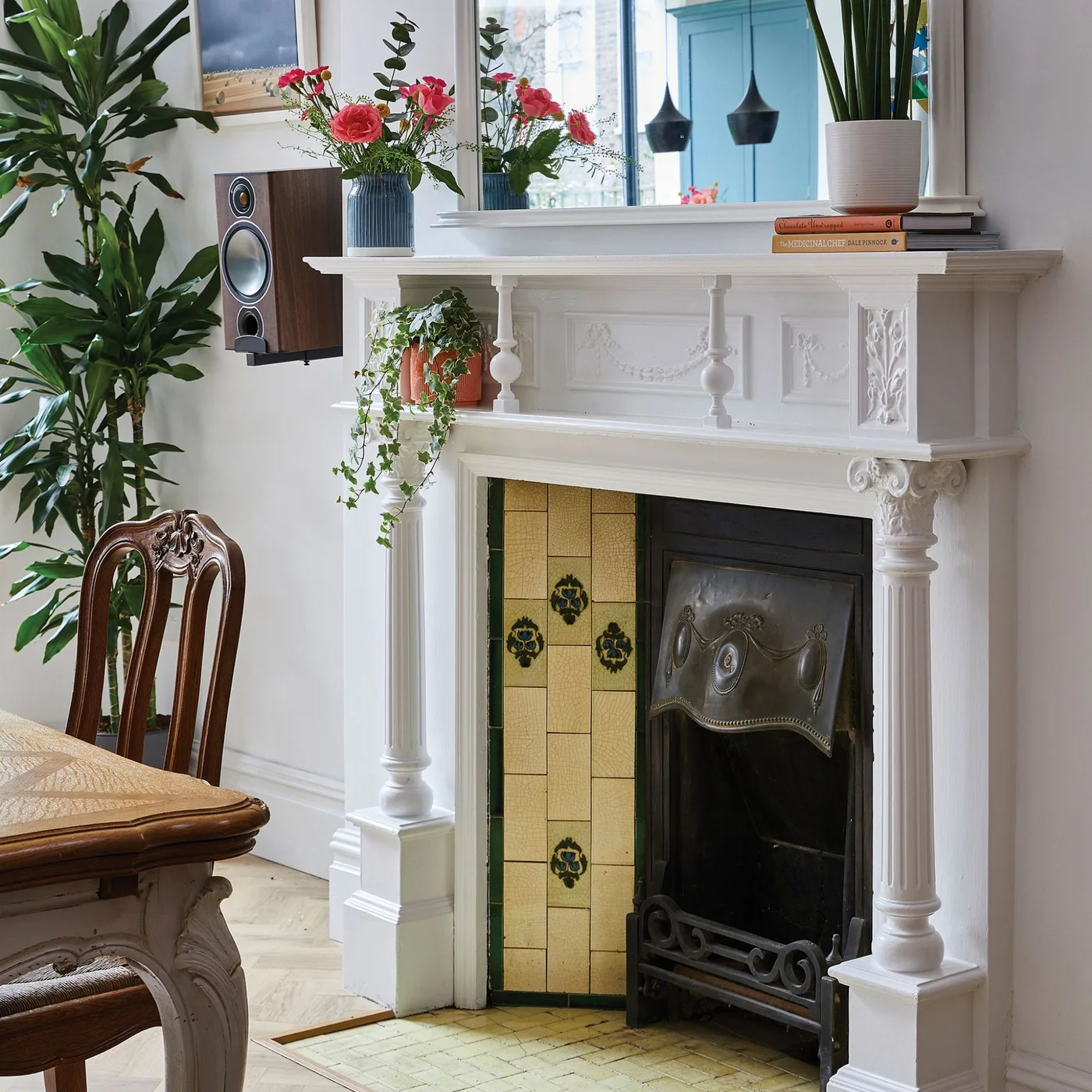 A white fireplace with turned columns and decorative panels frames yellow floral side tiles beside a dark insert.