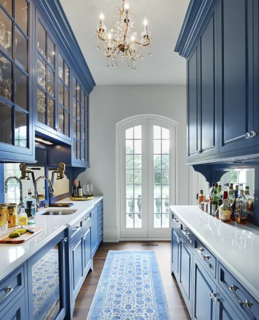 Blue cabinets run along both sides of a narrow kitchen beneath a chandelier.