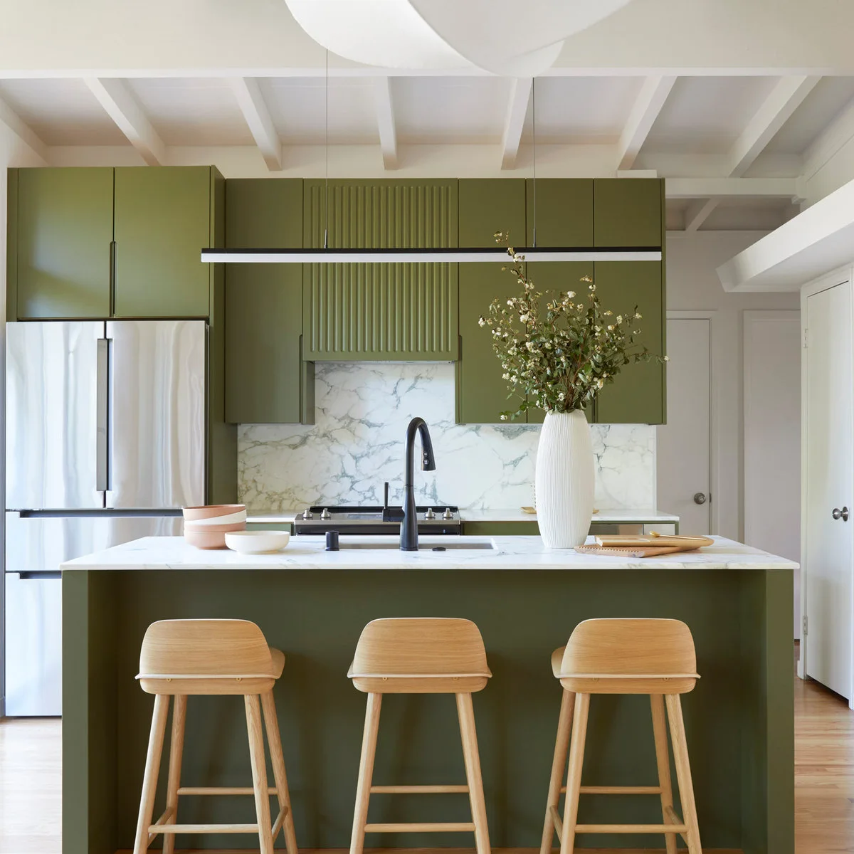 Olive kitchen with matching island, pale counters and three wooden stools