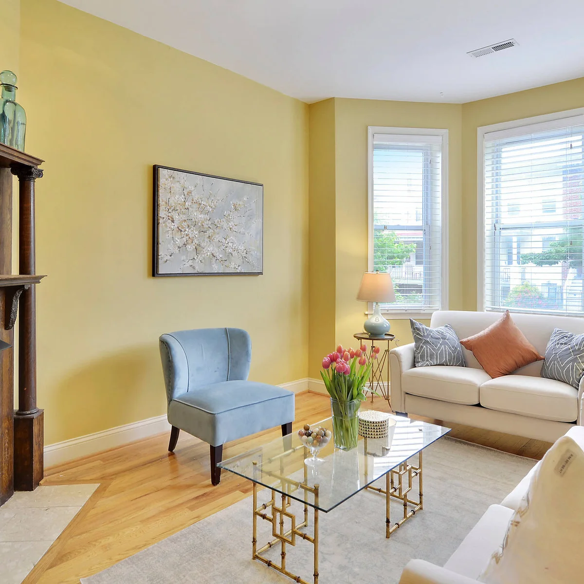 Living room with pale yellow walls, a white sofa, pale blue chair and glass coffee table