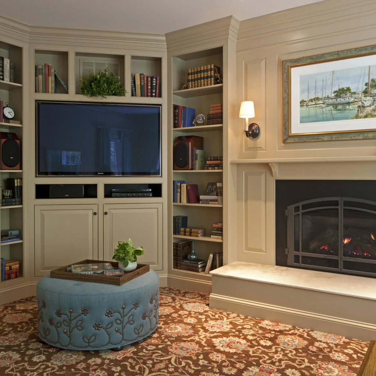 A television inside a painted cabinet to the left of a traditional fireplace with a framed sailing picture above the mantel.