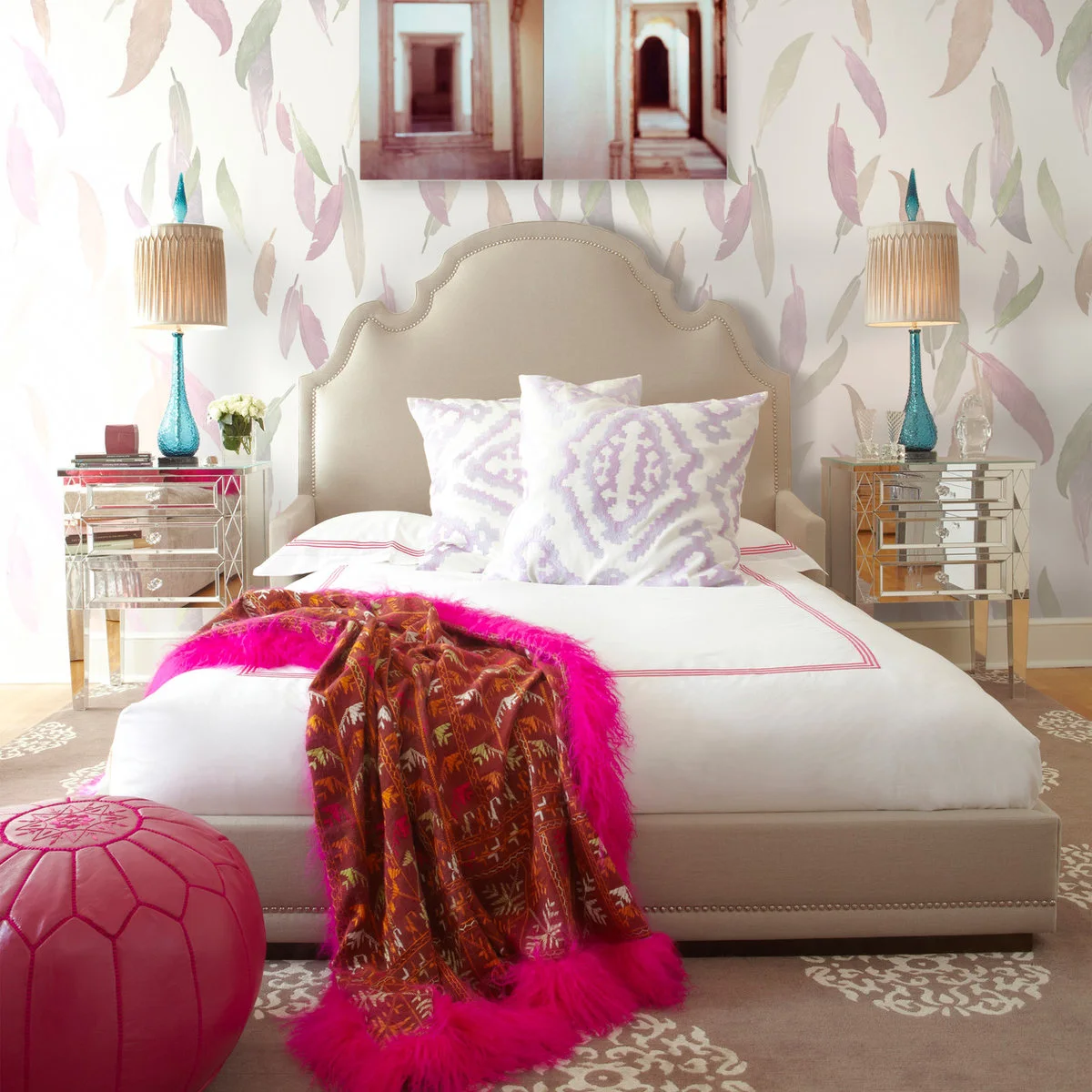 Mirrored bedside chests and turquoise lamps beside a bed against feather-patterned wallpaper