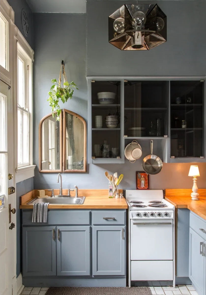 Small gray kitchen with glass-front upper cupboards and a pan and colander suspended above the stove