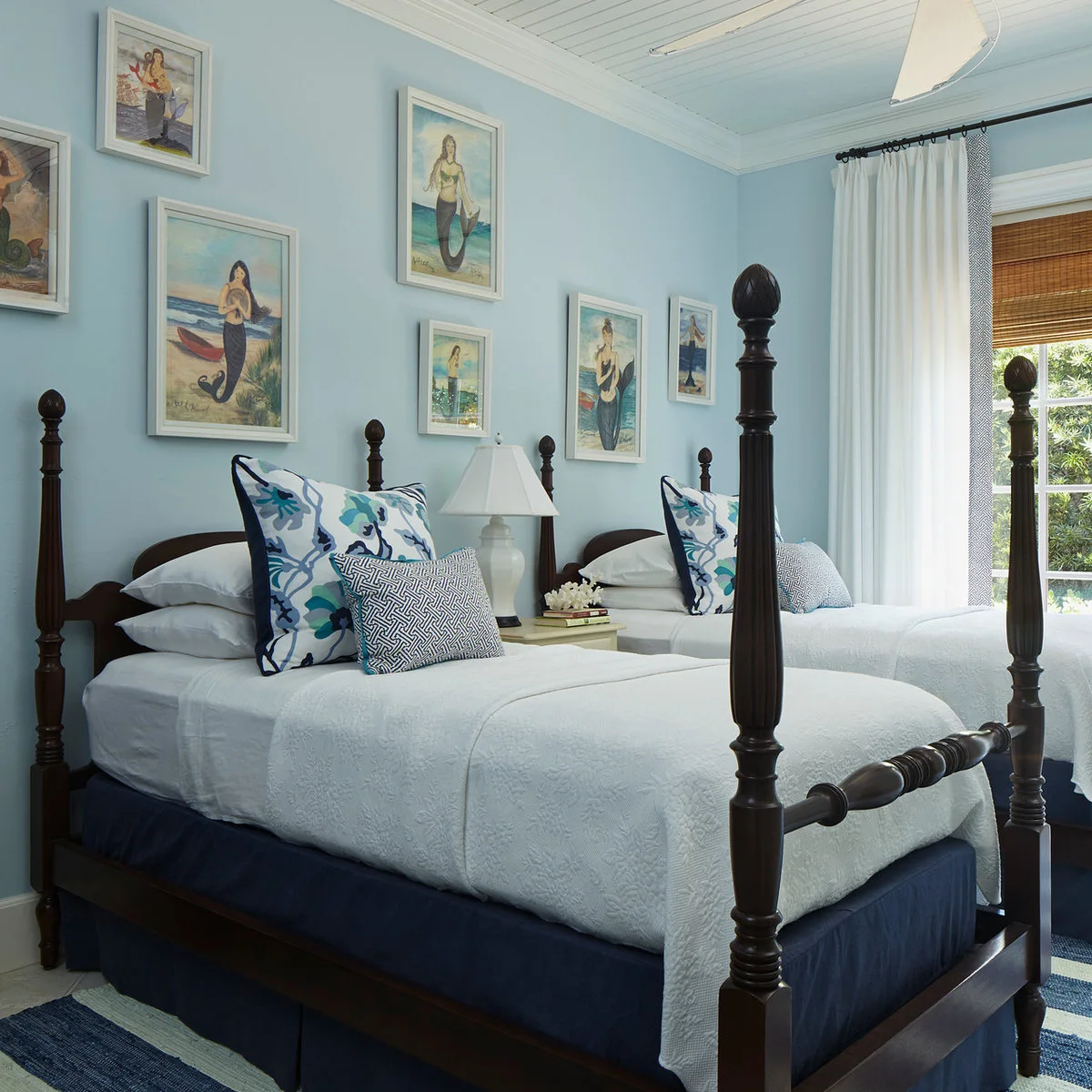 Two dark post beds with white covers, blue patterned cushions and a small pale shared bedside table