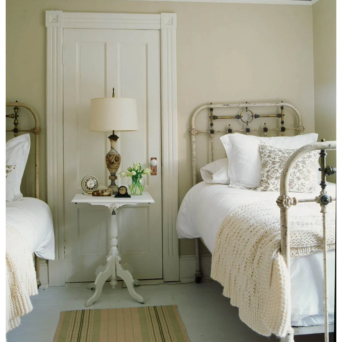 Two older-style pale metal beds with white bedding and a small shared pedestal table