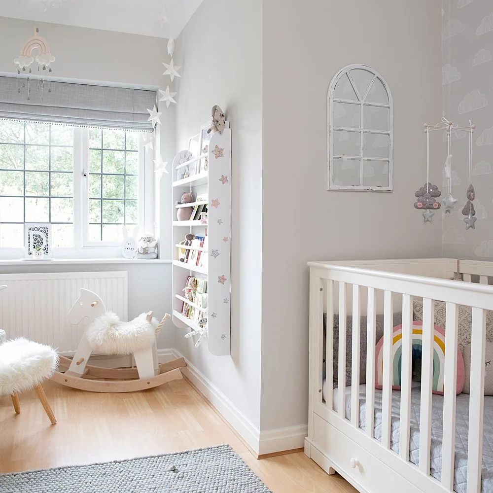 Pale crib beside open bookcase in gray-and-white nursery with arched wall piece and rocking horse near window.