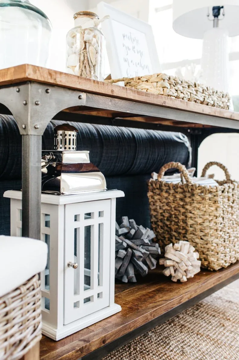 A white lantern, two decorative spheres and a woven basket occupy the lower shelf of a timber sofa console.