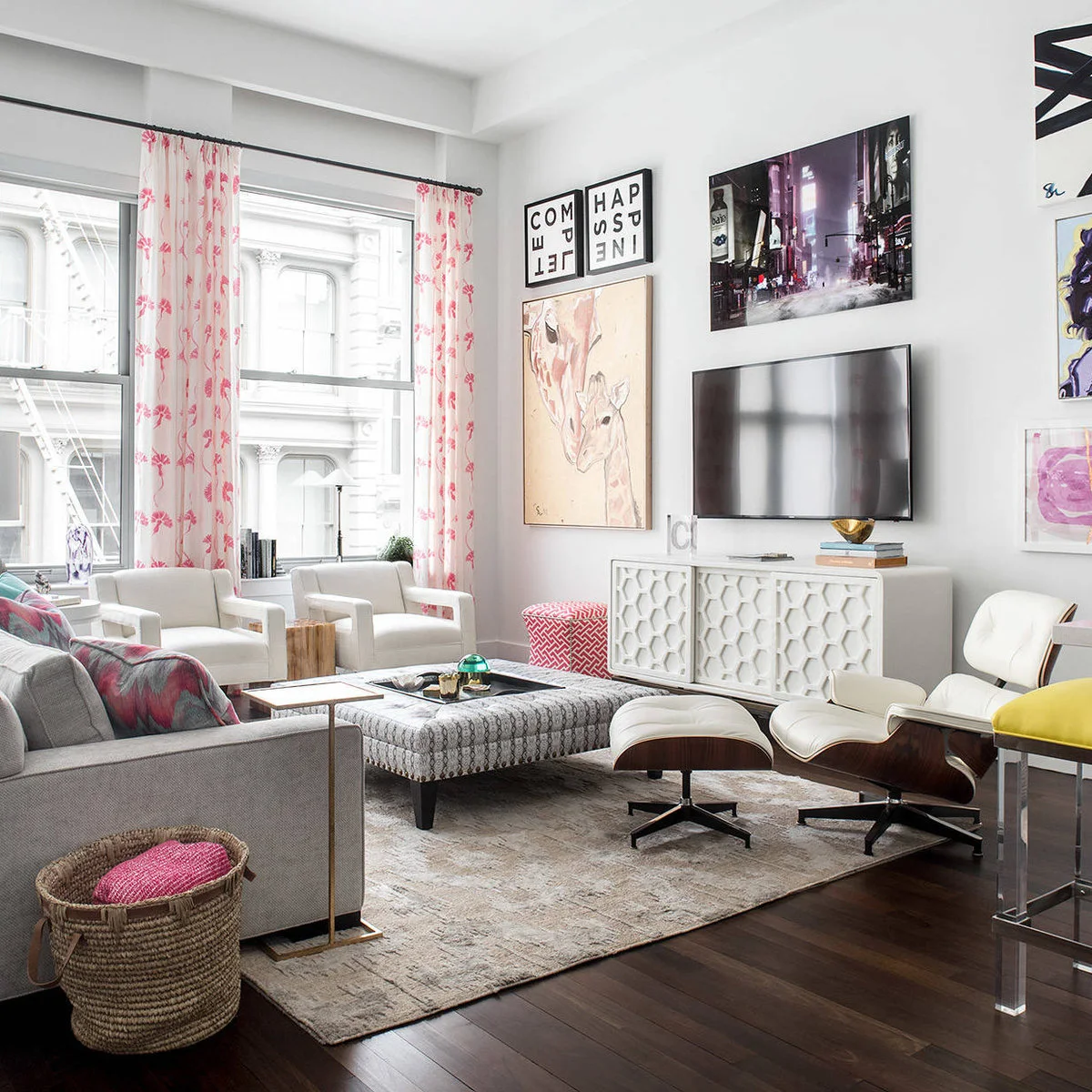Large city photograph above a television surrounded by smaller colorful pictures over a white cabinet.