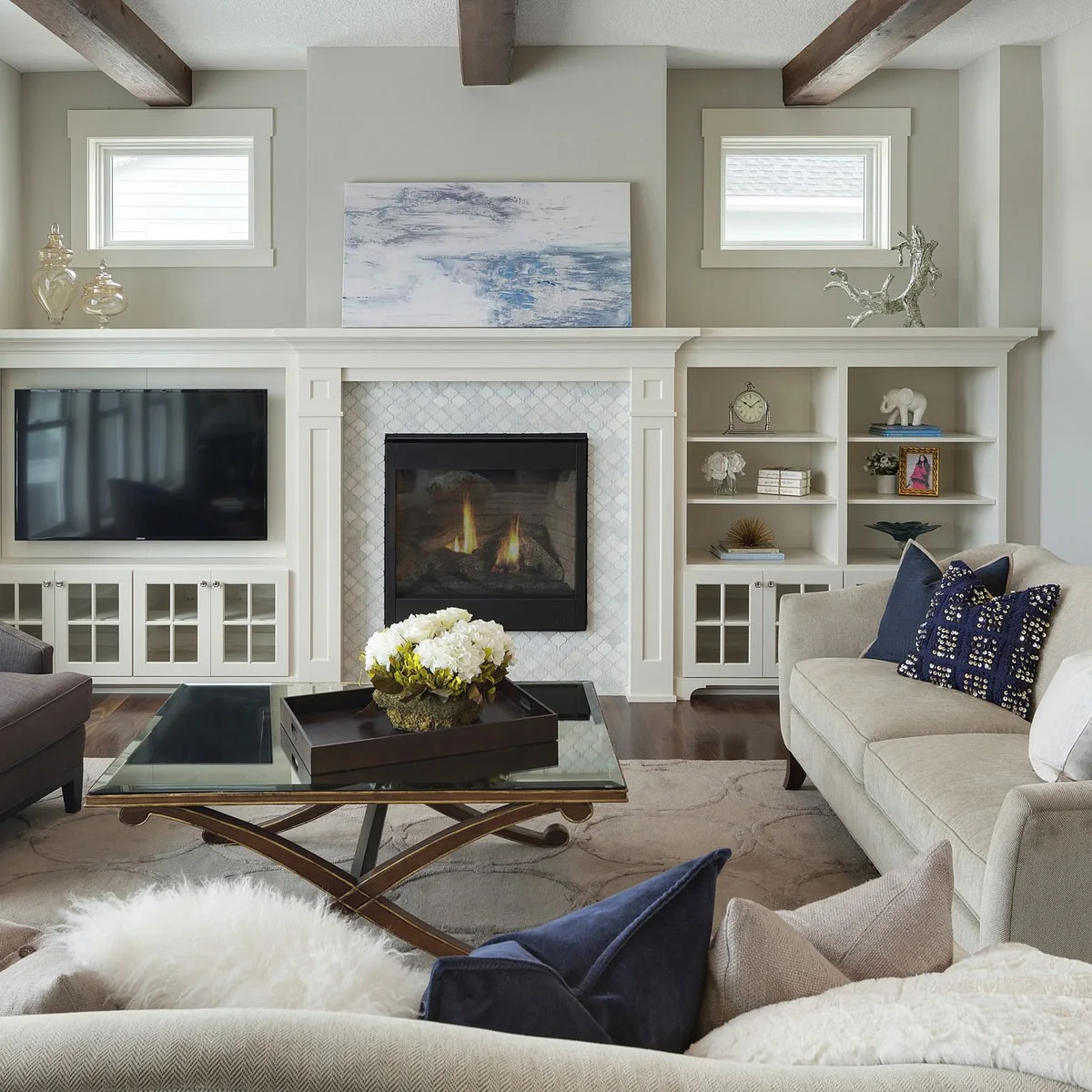 A television to the left of a patterned fireplace beneath one long white mantel, with shelves and glass-front cupboards.