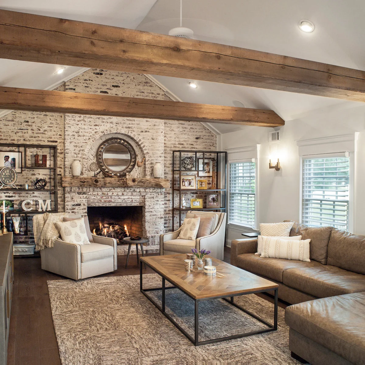 A brown sectional and two pale chairs surround a rectangular wood-topped table in a room with a brick fireplace.