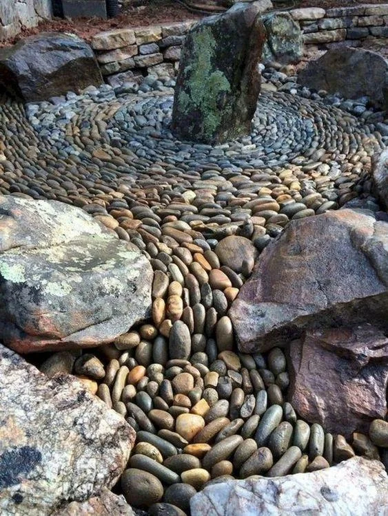 Rows of upright rounded pebbles curve around a central dark stone and larger surrounding rocks