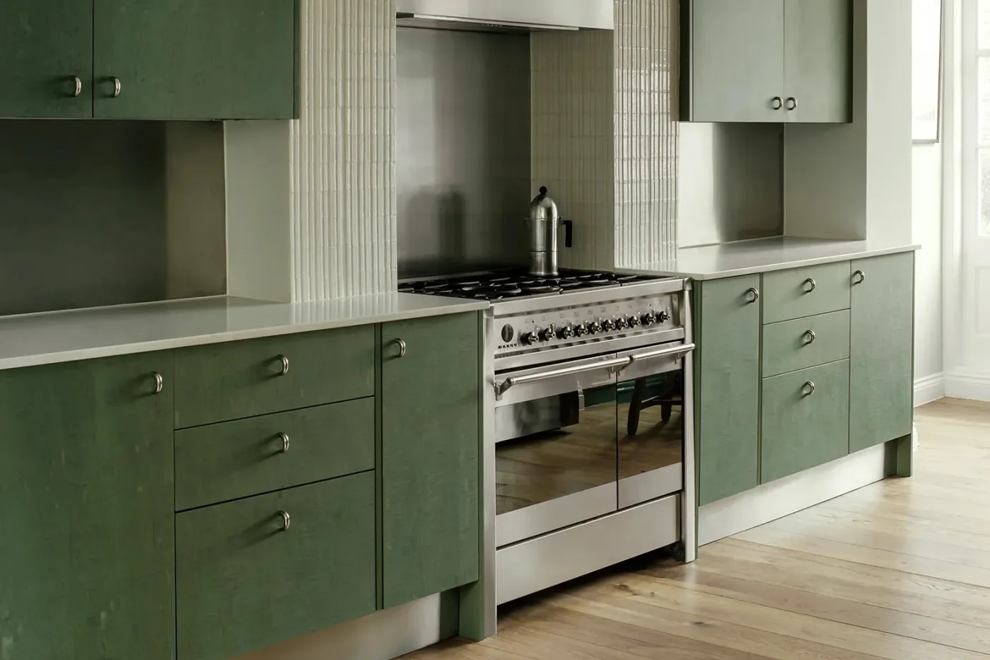 Green cabinets with visible grain and round metal pulls sit beside a pale fluted range surround and light countertops