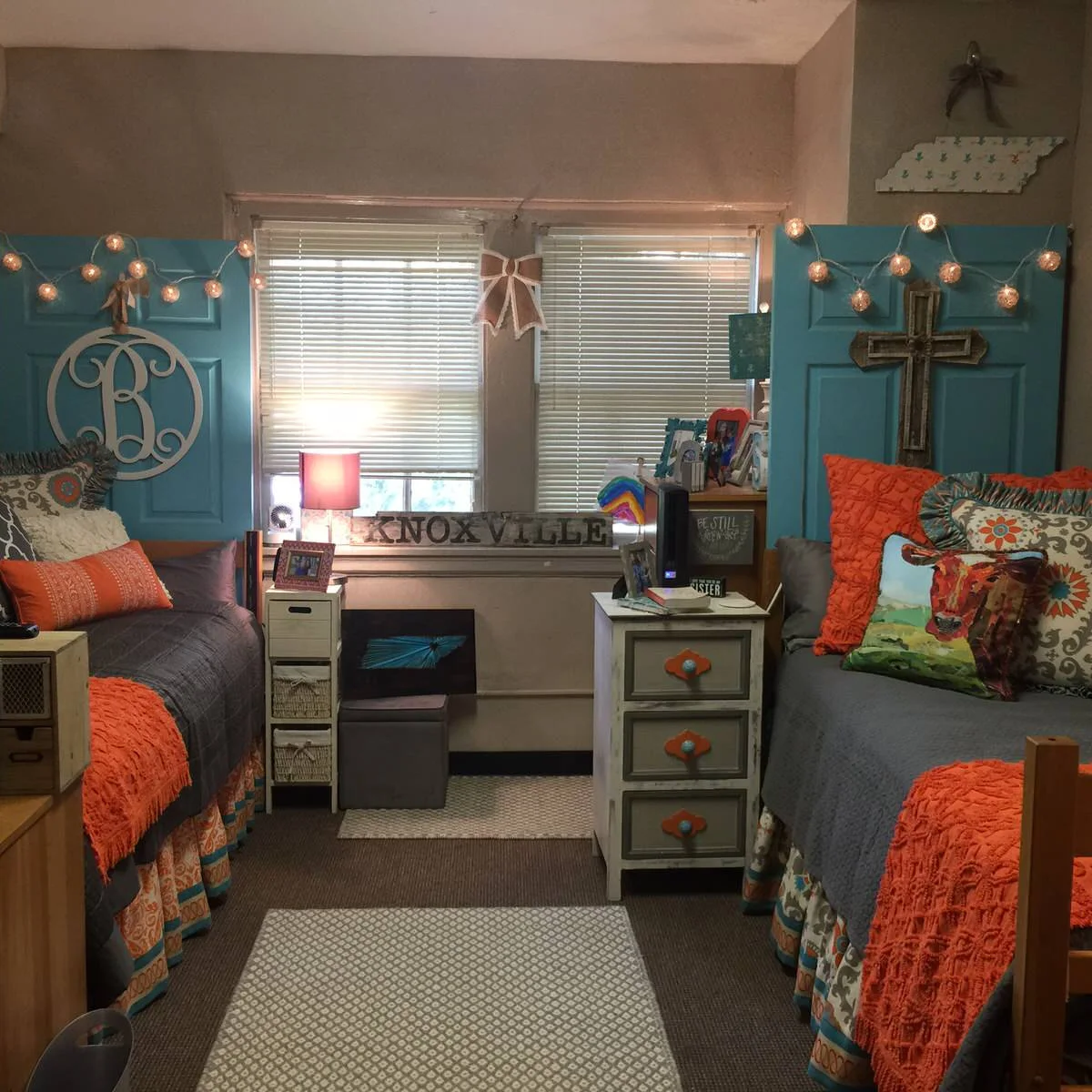 Shared dorm room with two raised beds, turquoise headboard panels, gray bedding and orange accents