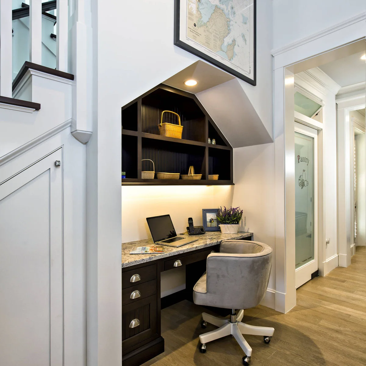 Under-stair desk with dark drawers, patterned pale top, illuminated shelving and a gray swivel chair