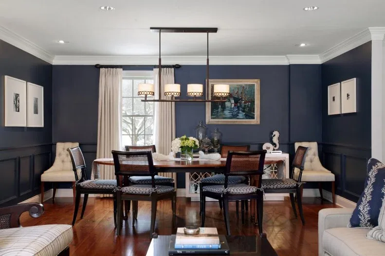 Navy dining room with dark open-backed chairs, pale upholstered end chairs, a wood table and a linear four-shade pendant