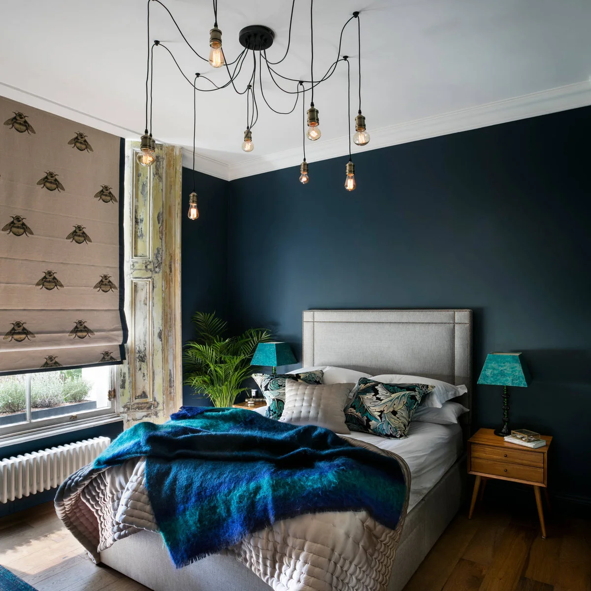 Deep blue bedroom with pale upholstered bed, blue throw and paired turquoise lamps