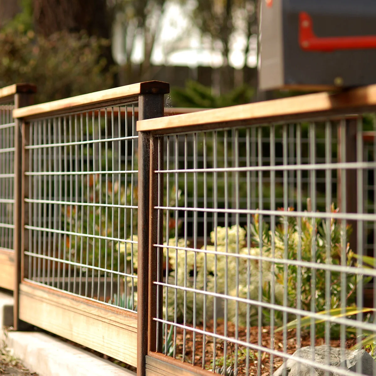 A fine metal grid fence with dark posts, a wood top rail and a broad wood board along the base.