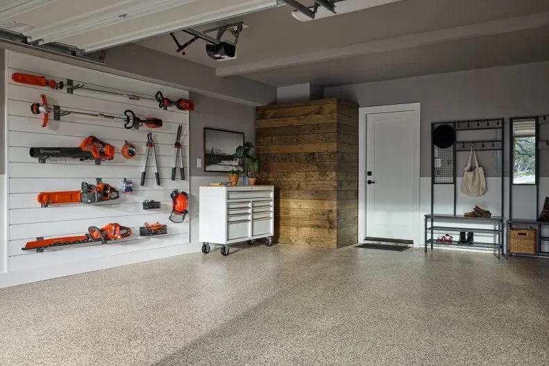 Garage with tool storage on one wall, a rolling cabinet, house-entry door and freestanding shoe benches.