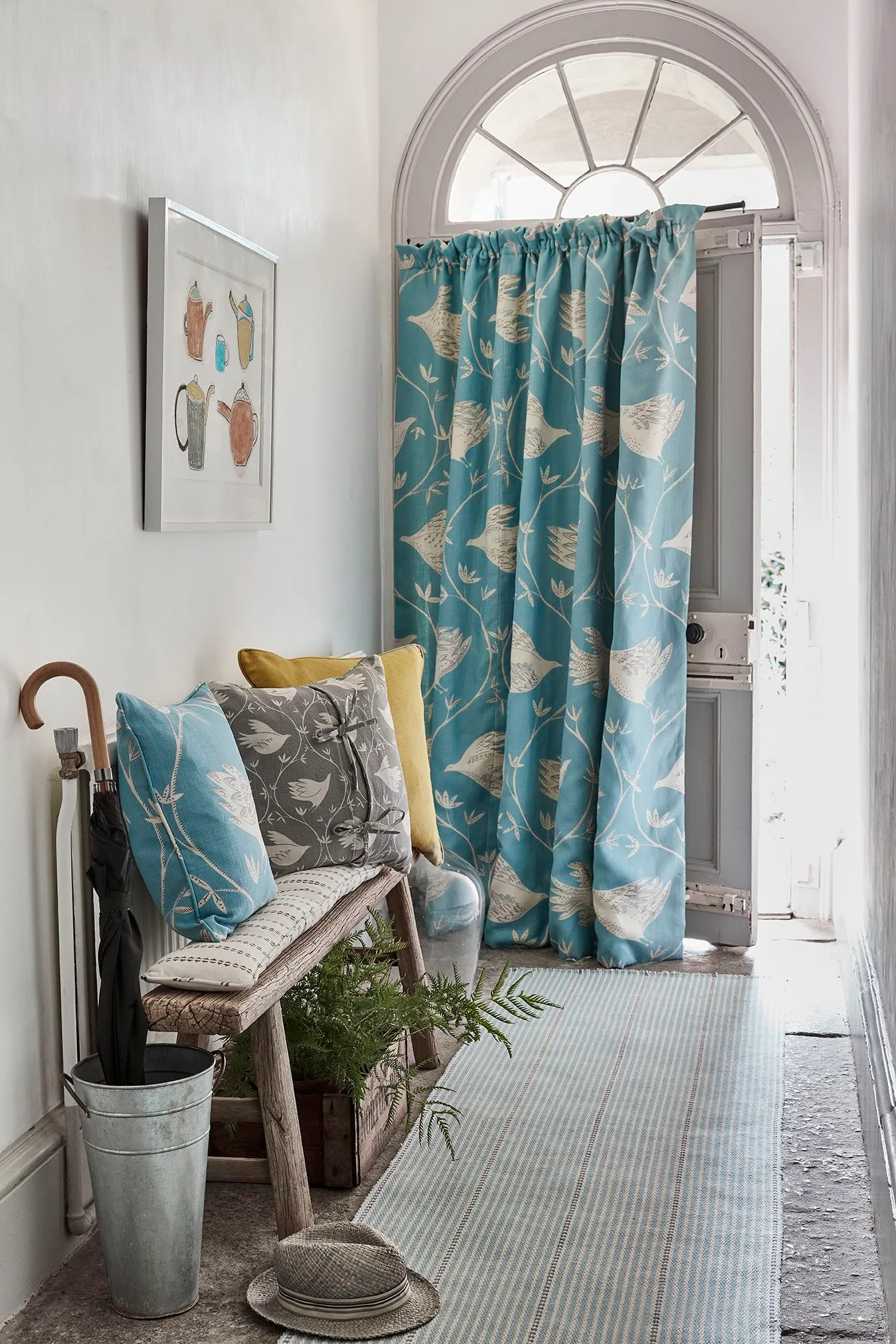 Traditional entrance with a blue bird-patterned door curtain, wooden bench, cushions and umbrella container.