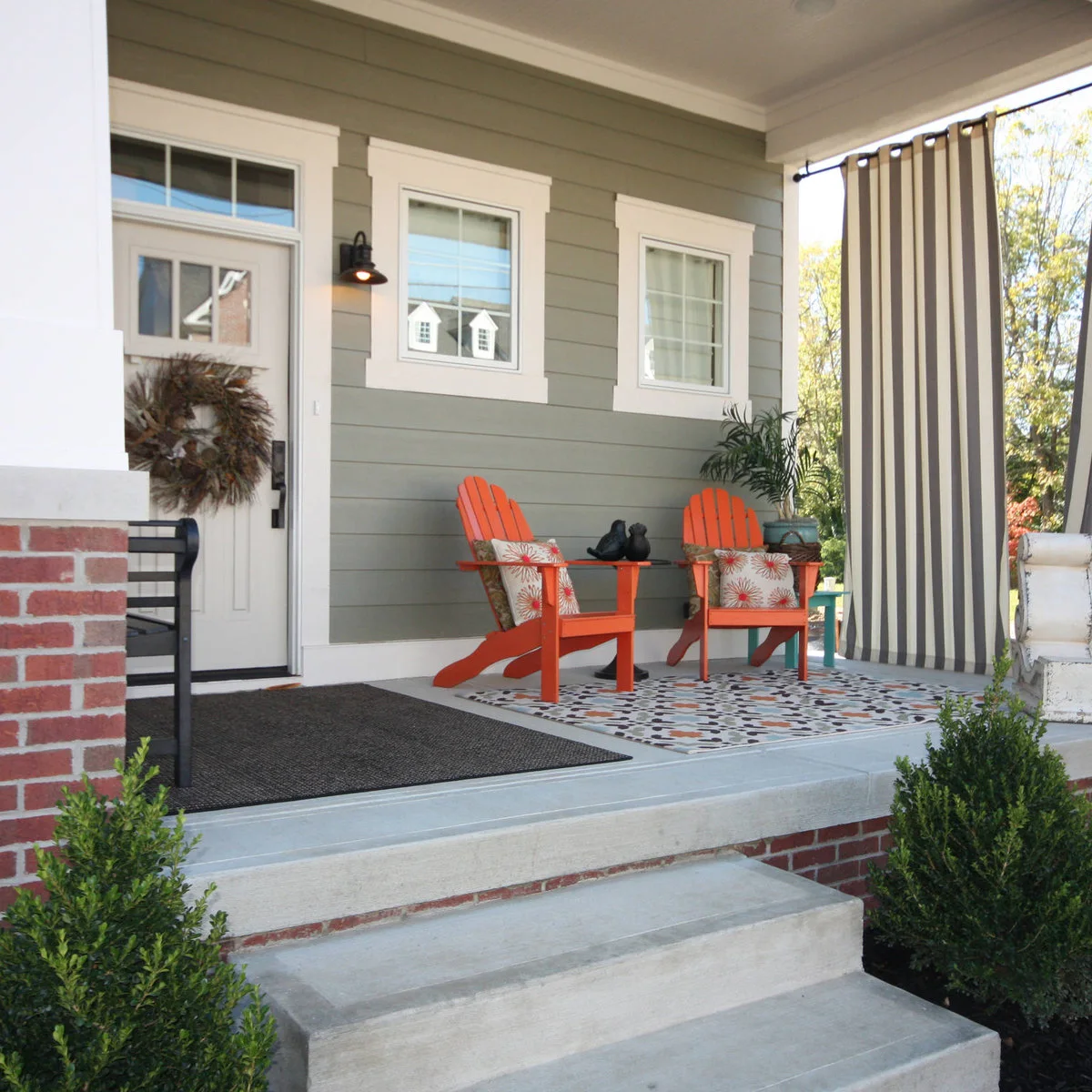 Two orange porch chairs on a patterned rug beside a front door and striped outdoor curtain