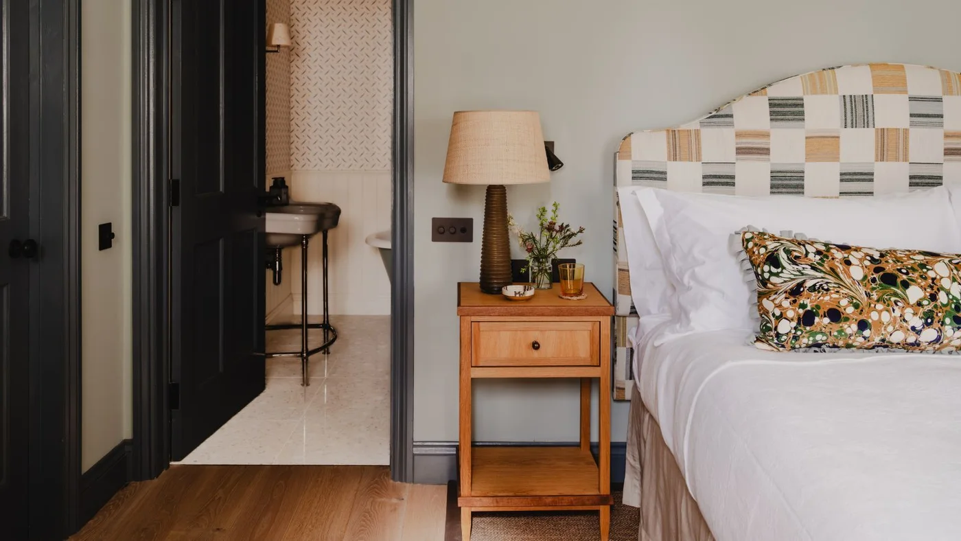 Pale blue-gray wall beside dark bedroom doors with a patterned headboard and wooden bedside table.