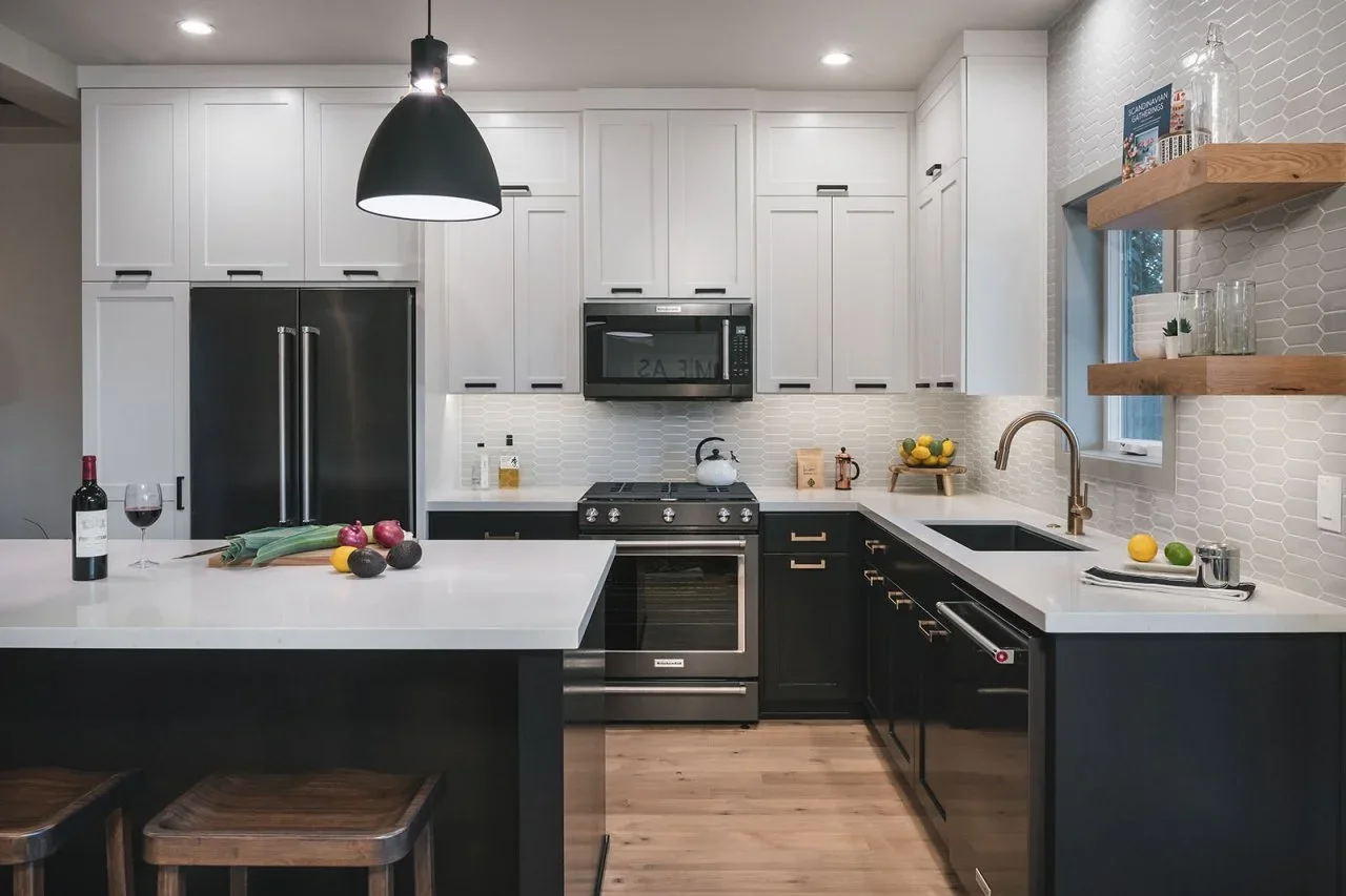Black lower cabinets and appliances contrast with white uppers and pale counters in a small kitchen with wood shelves beside the sink.