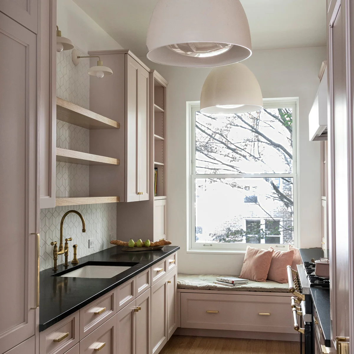 Pale pink galley kitchen with dark counters and a cushioned window seat at the end
