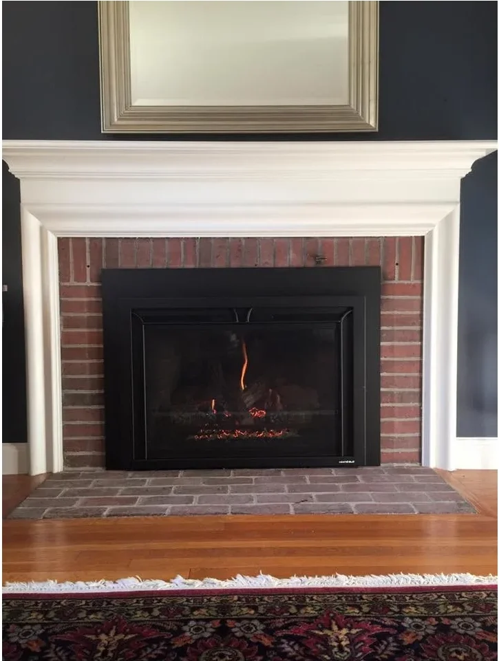 A pale traditional mantel surrounds red brick and a dark fireplace insert against a deep blue-gray wall.