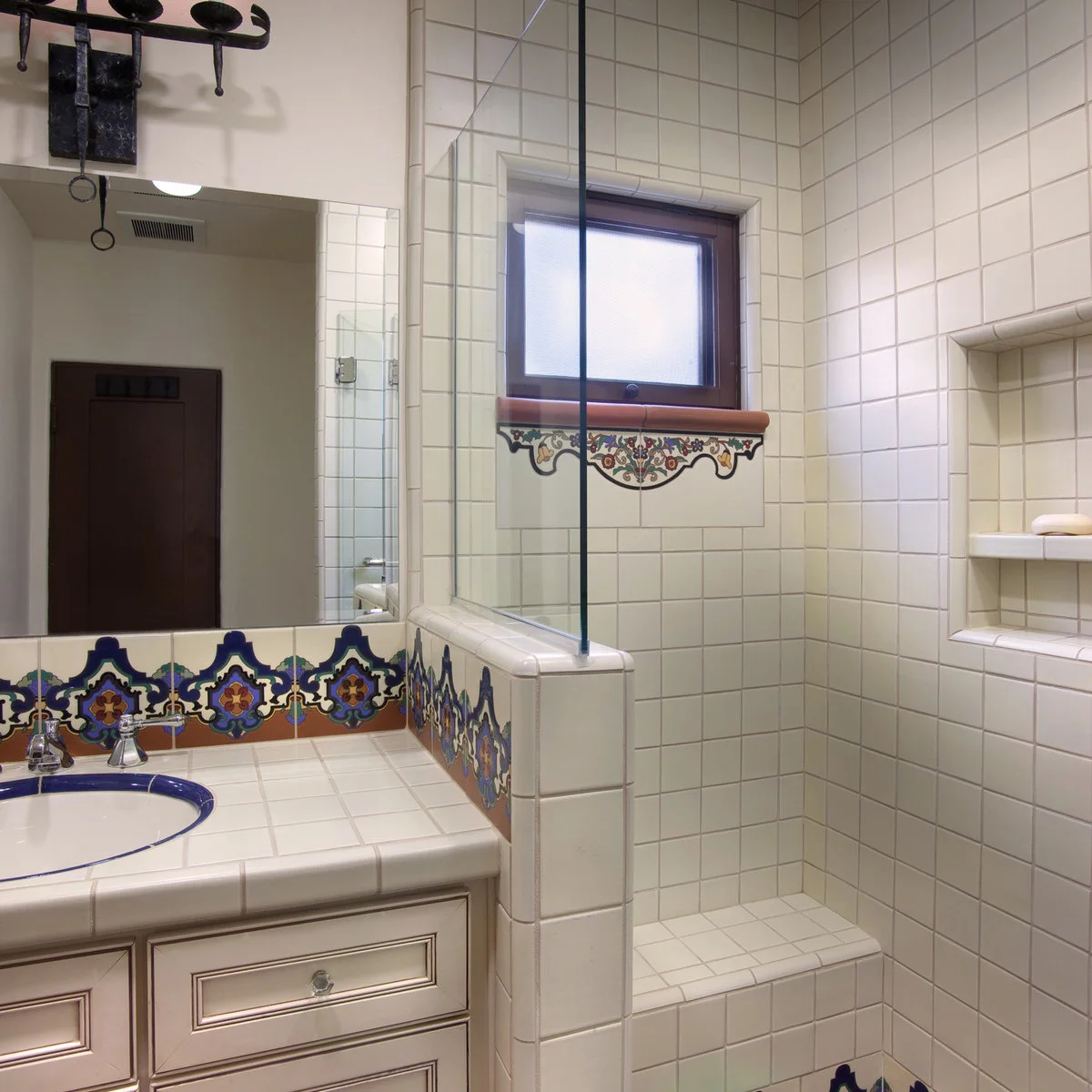 White square-tiled bathroom with a blue-and-yellow decorative backsplash and a patterned window accent