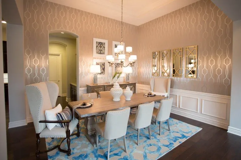Pale pink dining room with geometric wallpaper, light chairs, tall wing-shaped end seats, a wood table and a blue patterned rug