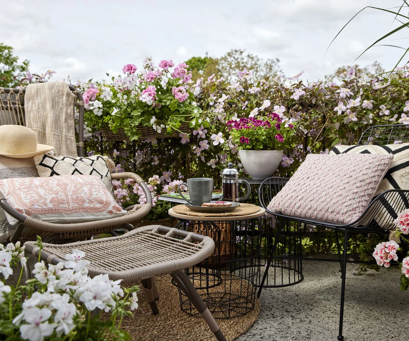Pink and white flowering containers form a leafy backdrop behind two outdoor chairs