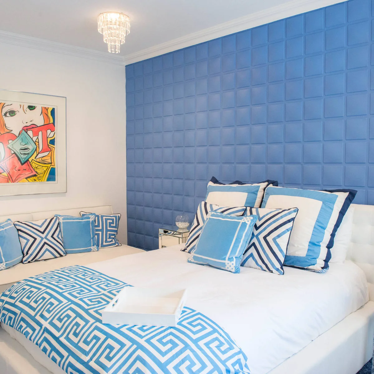 Blue paneled bedroom wall behind a white bed with blue-and-white bordered bedding and a white bench.